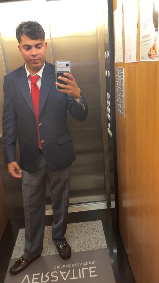 Jai Agarwal in a navy blazer and red tie, in the mirror of a hotel lift on signing day